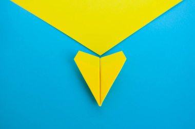 Sarı kağıttan uçağın mavi arka planda uçtuğu üst görüntüyü kapat..