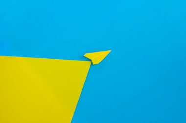 Mavi arka plan üzerinde uçan sarı kağıt uçağın açılı görüntüsü.