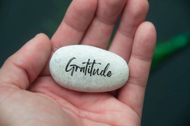 Hand holding Zen stone with Gratitude text engraved on the stone. Gratitude and peace concept clipart