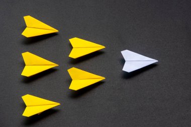 Beyaz kağıt uçak origamisinin üst görüntüsü. Mavi, siyah arka planda sarı uçaklar. Liderlik becerileri kavramı.