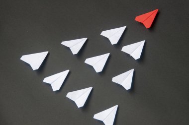 Kırmızı kağıttan uçak origamisinin üst görüntüsü mavi arka planda beyaz uçaklara öncülük ediyor. Liderlik becerileri kavramı.