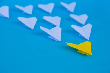 Sarı kağıttan uçak origamisinin yakın görüntüsü beyaz uçaklara öncülük ediyor ve yazı için özel alan yaratıyor. İş ve Liderlik becerileri kavramı.