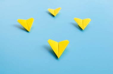 Sarı kağıttan uçak origamisinin düz görüntüsü diğer sarı uçakları mavi arka planda, kişiselleştirilebilir metin alanı ile yönlendiriyor. İş ve Liderlik becerileri kavramı.