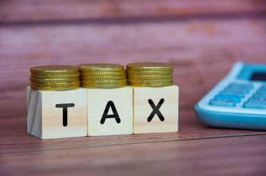 Altın sikkeler ve hesap makinesi arkaplanlı tahta küp hakkında vergilendirme sözcüğü.