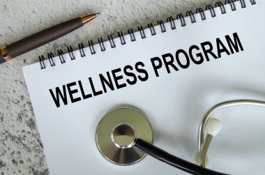 Tahta masa arkasında steteskop bulunan beyaz kağıt not defterindeki Sağlık Programı metninin üst görüntüsü. Sağlık ve Tıp Konsepti