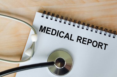 Tahta masa zemininde steteskop bulunan beyaz kağıt not defterine yazılmış tıbbi rapor metninin üst görüntüsü. Sağlık ve Tıp Konsepti