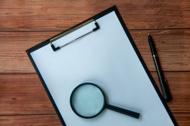 Üzerinde büyüteç ve siyah kalem olan beyaz kağıt panonun üst görüntüsü. Boşluk konseptini kopyala