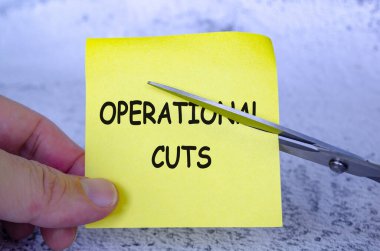 Üzerinde Operasyonel Kesikler yazan sarı yapışkan bir not tutarken, bir makas da notu kesiyor.