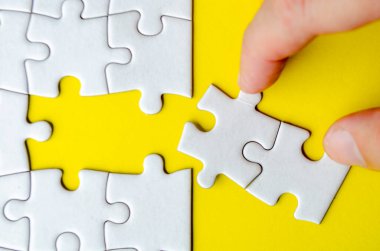 Beyaz yapbozları birleştirmekten çekilen el görüntüsü sarı kapaklı arka plandaki orijinal konumuna getiriliyor.