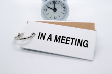 Beyaz arkaplanda alarm saati olan beyaz not defterindeki bir toplantı metninde. Ofis kavramından uzakta.