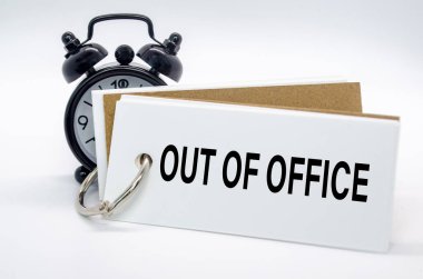 Ofis dışı mesajı beyaz arka planda alarm saati olan beyaz not defterine. Ofis kavramından uzakta.