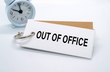 Ofis dışı mesajı beyaz arka planda alarm saati olan beyaz not defterine. Ofis kavramından uzakta.