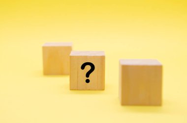 Sarı arka planda siyah soru işareti olan açık tahta bir blok..