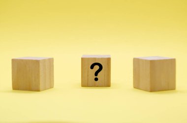 Soluk yüzey üzerinde soru işaretleri olan üç hafif tahta blok ve sarı zemin.