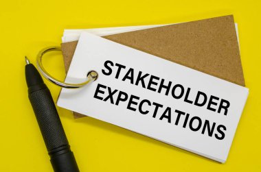 Beyaz arkaplanda klipsli STAKEHOLDER Beklentileri etiketli küçük defter.