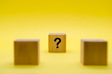 Sarı arka planda soru işaretleri olan iki tahta küp..