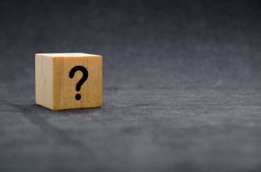 Karanlık bir yüzeyde soru işareti olan bir tahta blok..