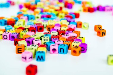 Beyaz bir yüzeye dağılmış alfabe harfleri ile canlı, çok renkli yarı saydam küplerin yakın görüntüsü eğlenceli ve eğitici bir düzenleme oluşturur..