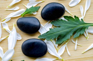 Bambu hasırının üzerine yerleştirilmiş yeşil yapraklı üç taş. Metin için özelleştirilebilir alanı olan doğal titreşim..