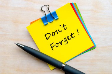 Sarı not defterine, tahta masaya yerleştirilmiş metal klipsli el yazısını unutma.