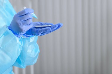 Doctor's hands performing antigen analisys of the fluid sample while wearing full personal protective equipment