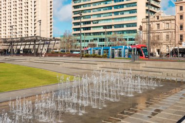 Adelaide City, South Australia - August 19, 2019: Victoria Square fountain on a bright day with Adelaide Metro tram driving past in the background