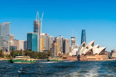 Sydney, Avustralya - 17 Nisan 2022: Sydney Opera Binası ve feribotlar güneşli bir günde modern Sydney City silueti üzerinden geçiyor