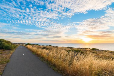 O 'Sullivan Sahili bisiklet yolu kıyı şeridi boyunca, gün batımında deniz üzerinde bulutlarla, Güney Avustralya
