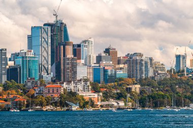 Sydney, Avustralya - 17 Nisan 2022: Sydney City şehir silueti panoramik görüntüsü açık bir günde mavi gökyüzü ve bulutlu feribot kalkışı