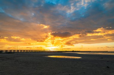 Moonta Körfezi sahilinde insanlar dramatik günbatımına karşı iskelede yürüyor, Güney Avustralya