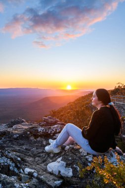 Woman sitting on edge of Reed Lookout cliff while enjoying sunset above Victoria Valley in Grampians mountains, Victoria, Australia clipart