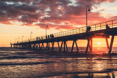 Glenelg Sahili İskelesi 'nde insanlar gün batımında Güney Avustralya' da geziniyor.