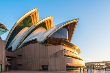 Sydney, Avustralya - 20 Nisan 2022: Konser salonu ve tiyatro ile Sydney Opera Binası 'nın günbatımında gezinen insanların güzel manzarası
