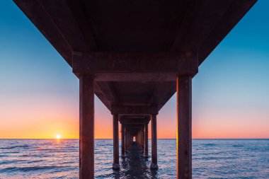 Brighton Jetty 'nin altından yaz akşamları gün batımında sahilde dururken, Güney Avustralya' yı izleyin.