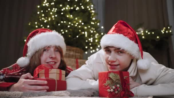 年轻人把头靠在装有新年礼物的盒子上躺在地上 他们相互望着对方 然后回头看相机 圣诞假期的概念 — 图库视频影像
