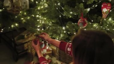Sıcak bir ev ortamında, genç bir kız tek başına bir Noel ağacı süsler. Güzel Noel oyuncakları. Yeni yıl gecesi.