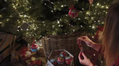 Ev ortamında, genç bir kız bir Noel ağacı süsler. Eller yakın çekim. Yeni yıl kutlaması konsepti.