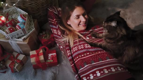 新年の雰囲気 お気に入りの猫の会社の若い女性がクリスマスツリーの下に横たわっている クリスマスのお祝いの概念 スローモーション — ストック動画