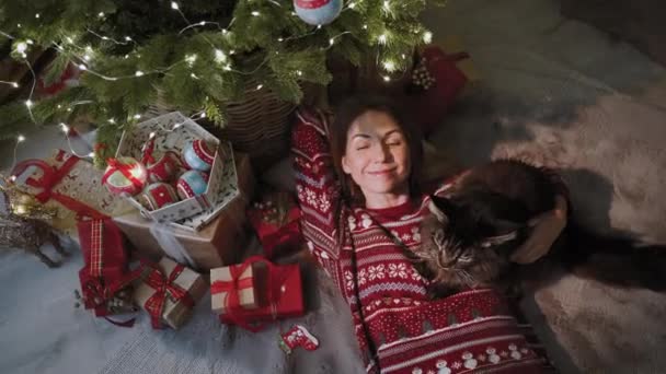 新年の雰囲気の中で 美しい猫の会社では かわいい女性がクリスマスツリーの下に横たわっており この瞬間を楽しんでいます クリスマスツリーの周りには 家族全員のための多くの贈り物があります — ストック動画