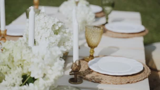 絶妙な料理 ろうそく 明るい花で装飾されたオープンエアガーデンには美しくセットされたテーブルがあります カメラはテーブルに何があるかを詳細に示しています — ストック動画