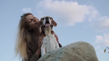 Bir kadın bir köpeği okşuyor ve gülümseyerek ona bakıyor. Bir kız gün batımının ve evcil hayvanının arkadaşlığının tadını çıkarıyor. 