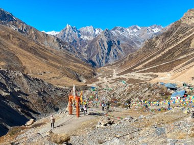 Om Parvat 'a giden yolda bayraklı ve tapınak çanlı kutsal kapı. Arka planda yılan şeklinde bir dağ olan Sheshnag Parvat