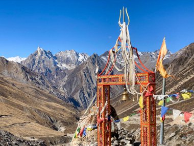 Om Parvat 'a giden yolda bayraklı ve tapınak çanlı kutsal kapı. Arka planda yılan şeklinde bir dağ olan Sheshnag Parvat