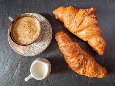 Bir fincan kahve ve mini süt bardağı yanında hamur işi, basit kahvaltı konsepti.