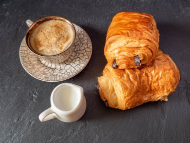 Bir fincan kahve ve mini süt bardağı yanında hamur işi, basit kahvaltı konsepti.