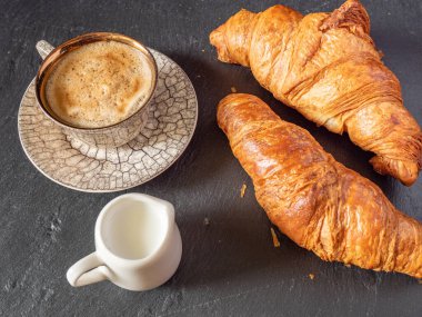 Bir fincan kahve ve mini süt bardağı yanında hamur işi, basit kahvaltı konsepti.