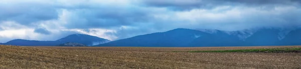Panoramic view of mountains with storm clouds and crop fields in foreground in autumn