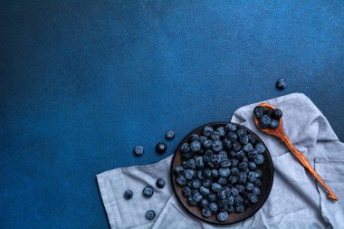 Plate with fresh blueberries on a blue background. Fresh berries and wooden spoon.