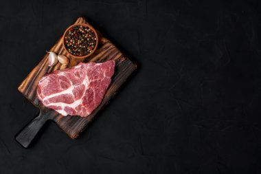 Raw pork steak on a wooden cutting board. Meat, dry pepper mixture, garlic on a black background. View from above