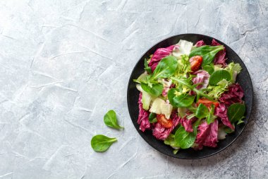 Kırmızı lahanalı salata, salatalık, domates ve roka gri beton arka planda siyah bir tabakta. Üst görünüm, alanı kopyala.